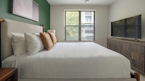 Un dormitorio con una cama grande, televisión y ventana con persianas.