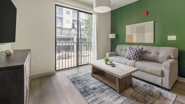 Una sala de estar moderna con un sofá, una mesa de centro y vistas a un balcón exterior a través de una puerta corrediza.