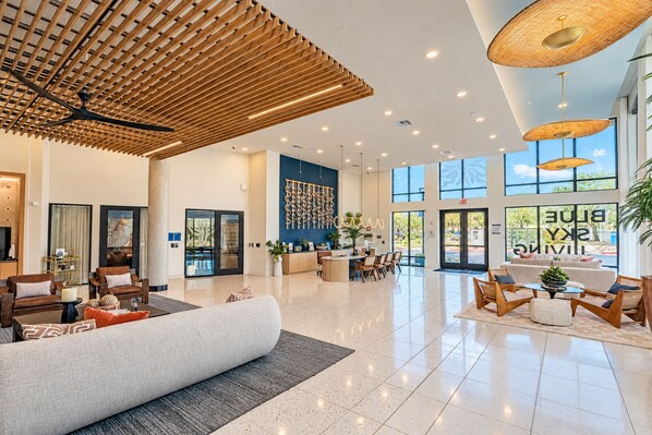 Un hall de hotel espacioso con techo alto, una recepción, zonas de estar y grandes ventanales con vistas al exterior.