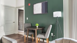 A dining area with a round table, two chairs, a potted plant, a floor lamp, and a painting on the wall. - Landing | Spectacular 2BD, Gym (Birmingham)