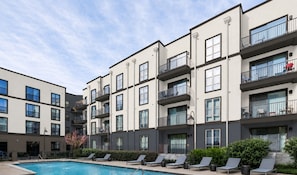 A modern multi-story residential building with a swimming pool and lounge chairs. - Landing | Amazing 2BD, Gym (Birmingham)
