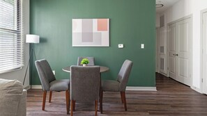 A dining area with a round table, two chairs, a potted plant, and a wall-mounted abstract art piece. - Landing | Amazing 2BD, Gym (Birmingham)