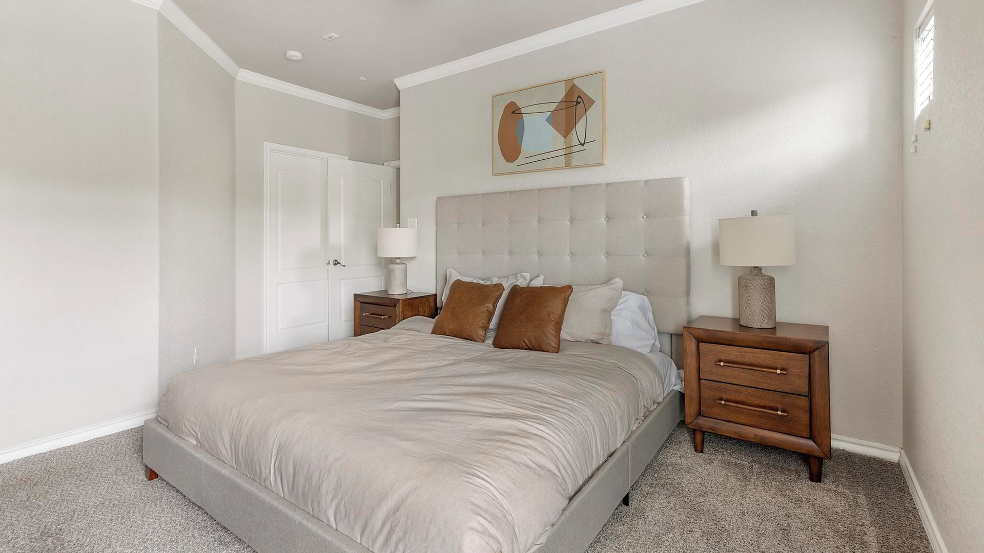 Een slaapkamer met een groot bed, twee nachtkastjes, een deur en een kunstwerk aan de muur.