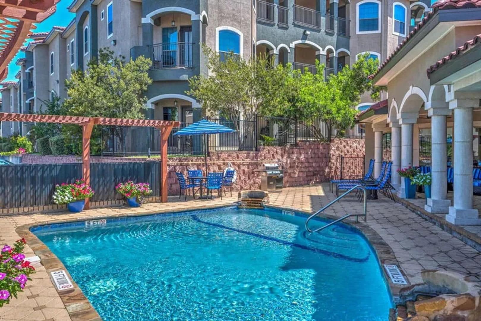 A swimming pool with a stone border, surrounded by outdoor seating and a pergola.