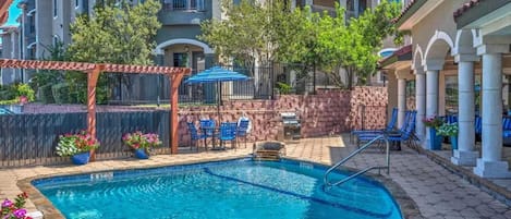 Une piscine bordée de pierres, entourée d’un espace de détente extérieur et agrémentée d’une pergola.