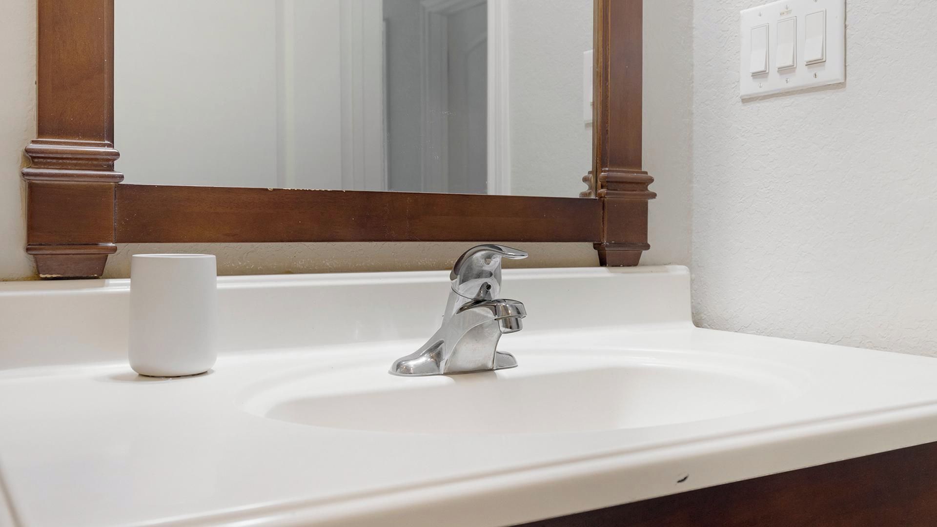 A bathroom with a white sink, a mirror with wooden frame, and a white cup on the counter.