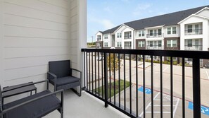 A balcony with two chairs, a view of a parking lot, and multi-story buildings in the background. - Landing | Modern 1BD in Whitestone (Fort Worth)