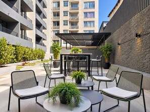 An outdoor seating area with tables and chairs, surrounded by potted plants and a building in the background. - Estudio Metro Toesca y Club Hípico (Santiago)
