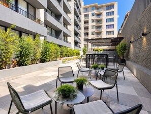 A courtyard with outdoor seating, potted plants, and a view of a multi-story building. - Estudio Metro Toesca y Club Hípico (Santiago)