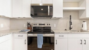 A modern kitchen with white cabinetry, a stainless steel microwave, an oven, and a sink. - Landing | Incredible 1BD in Whitestone (Fort Worth)