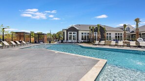A swimming pool with lounge chairs and a covered seating area, surrounded by buildings and palm trees. - Landing | Incredible 1BD in Whitestone (Fort Worth)
