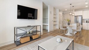 A modern living room with a flat-screen TV, a glass console table, and a dining area with a round table and chairs. - Landing | Incredible 1BD in Whitestone (Fort Worth)