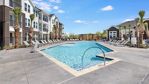 A rectangular swimming pool with a diving board, surrounded by lounge chairs and palm trees, adjacent to multi-story buildings. - Landing | Modern 1BD in Whitestone (Fort Worth)