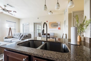 A modern kitchen with a double sink, granite countertop, and pendant lighting. - Landing | Incredible 2BD, Gym, Pool (Oxford)