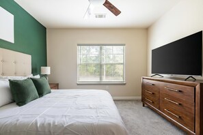A bedroom with a bed, a dresser, a television, and a window with blinds. - Landing | Modern 2BD, Pool, Gym (Oxford)