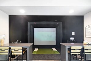 A room with a projector screen displaying 'FULL SWING SIMULATORS,' a small artificial turf area, and a desk with a computer. - Landing | Spectacular 2BD, Pool, Gym (Oxford)