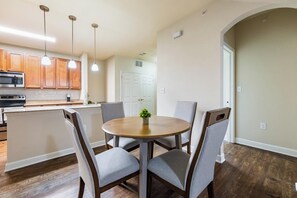 A modern kitchen with wooden cabinets, a microwave, and a dining area with a round table and four chairs. - Landing | Amazing 2BD, Gym, Pool (Oxford)
