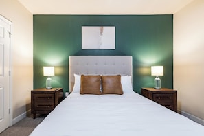 A hotel room with a large bed, two bedside tables with lamps, a green accent wall, and a simple artwork above the bed. - Landing | Amazing 2BD, Gym, Pool (Oxford)