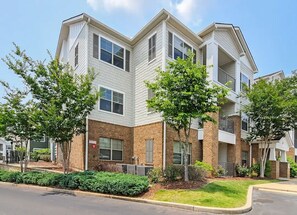 A multi-story residential building with a brick facade and white trim, featuring a corner entrance and a small front yard with landscaping. - Landing | Chic 3BD, Pool, Gym (Oxford)