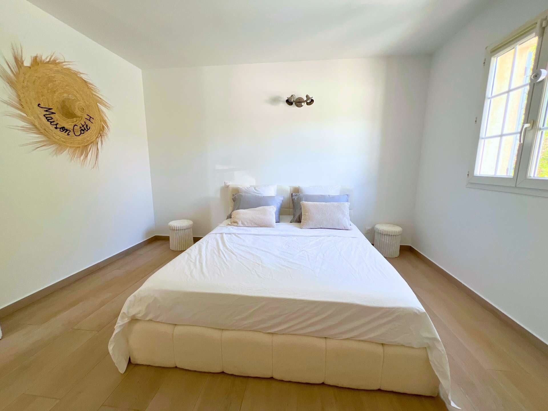 A bedroom with a large bed, two bedside tables, a wall-mounted light, and a window.