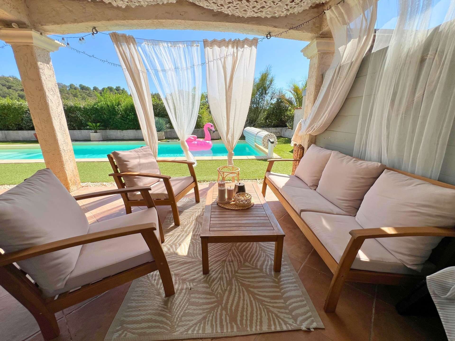 A covered outdoor seating area with a pool in the background.