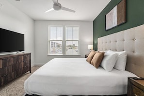 A bedroom with a large bed, a flat-screen TV, a ceiling fan, and a window with blinds. - Landing | Amazing 2BD, Gym (Pensacola)