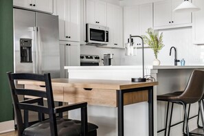 Eine moderne Küche mit weißen Schränken, Edelstahlgeräten, einem Holztisch und zwei Stühlen.
