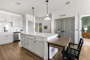 A modern kitchen with white cabinetry, a wooden dining table, and pendant lighting. - Landing | Amazing 2BD, Gym (Pensacola)