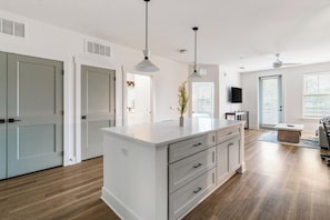A modern kitchen with a central island, pendant lighting, and a view to the dining area. - Landing | Modern 1BD, Gym (Pensacola)