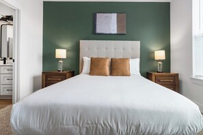 A hotel room with a large bed, two bedside tables with lamps, a green accent wall, and a painting above the bed. - Landing | Modern 1BD, Gym (Pensacola)