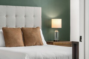 A neatly made bed with a tufted headboard, two brown pillows, and a bedside table with a lamp. - Landing | Modern 2BD, Gym (Pensacola)