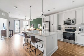 A modern kitchen with white cabinets, stainless steel appliances, and a central island with bar stools. - Landing | Stylish 1BD, Gym (Pensacola)