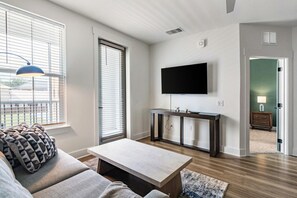 A modern living room with a sofa, coffee table, and a TV mounted on the wall. - Landing | Beautiful 1BD, Gym (Pensacola)