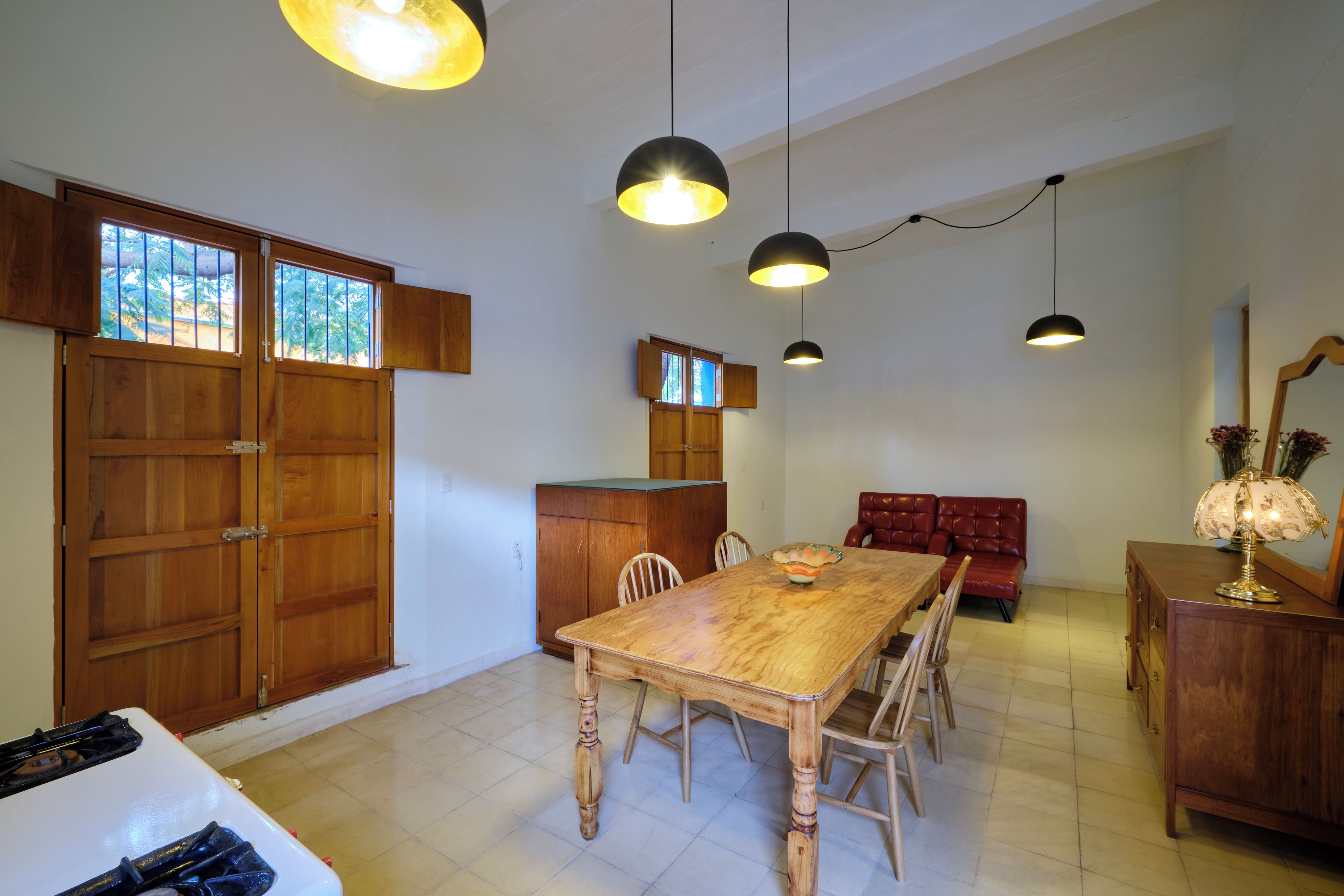 A spacious dining area with a wooden table and chairs, a red sofa, and pendant lighting.