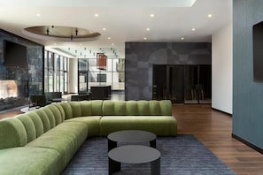 A modern interior with a green sectional sofa, two round tables, and a large window providing a view of the cityscape. - Landing | Chic 1BD, Pool, Gym (Green Bay)