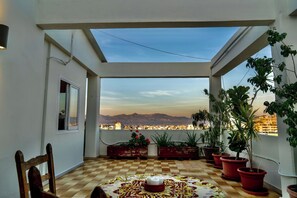 A balcony with a checkered floor, potted plants, a table with a candle, and a view of a cityscape and mountains. - Stylish 3BR w/ Huge Veranda and City View, Nicosia (Nicosia)