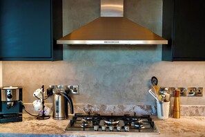 A kitchen with a gas stove, a coffee maker, a kettle, and a range hood. - Stylish 3BR w/ Huge Veranda and City View, Nicosia (Nicosia)