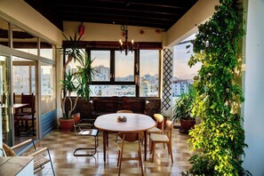 Un pati acollidor amb una taula rodona i caires, plantes en testos i una vista a la ciutat a través de grans finestres.