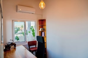 A room with a wooden table, a red chair, a bookshelf, and a large window with a view of buildings and trees. - Stylish 3BR w/ Huge Veranda and City View, Nicosia (Nicosia)