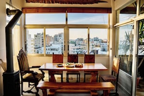A dining area with a table and chairs, a view of a cityscape through large windows, and a chimney. - Stylish 3BR w/ Huge Veranda and City View, Nicosia (Nicosia)