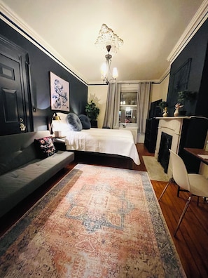 A bedroom with a bed, a sofa, a desk, a chair, a fireplace, and a large rug. - Comfortable, Super Clean & Close to NYC (Hoboken)
