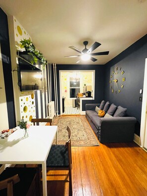 A modern living room with a sofa, a dining table, and a kitchen in the background. - Comfortable, Super Clean & Close to NYC (Hoboken)