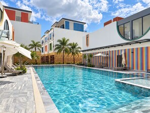A swimming pool with lounge chairs and umbrellas, surrounded by modern buildings with colorful facades.