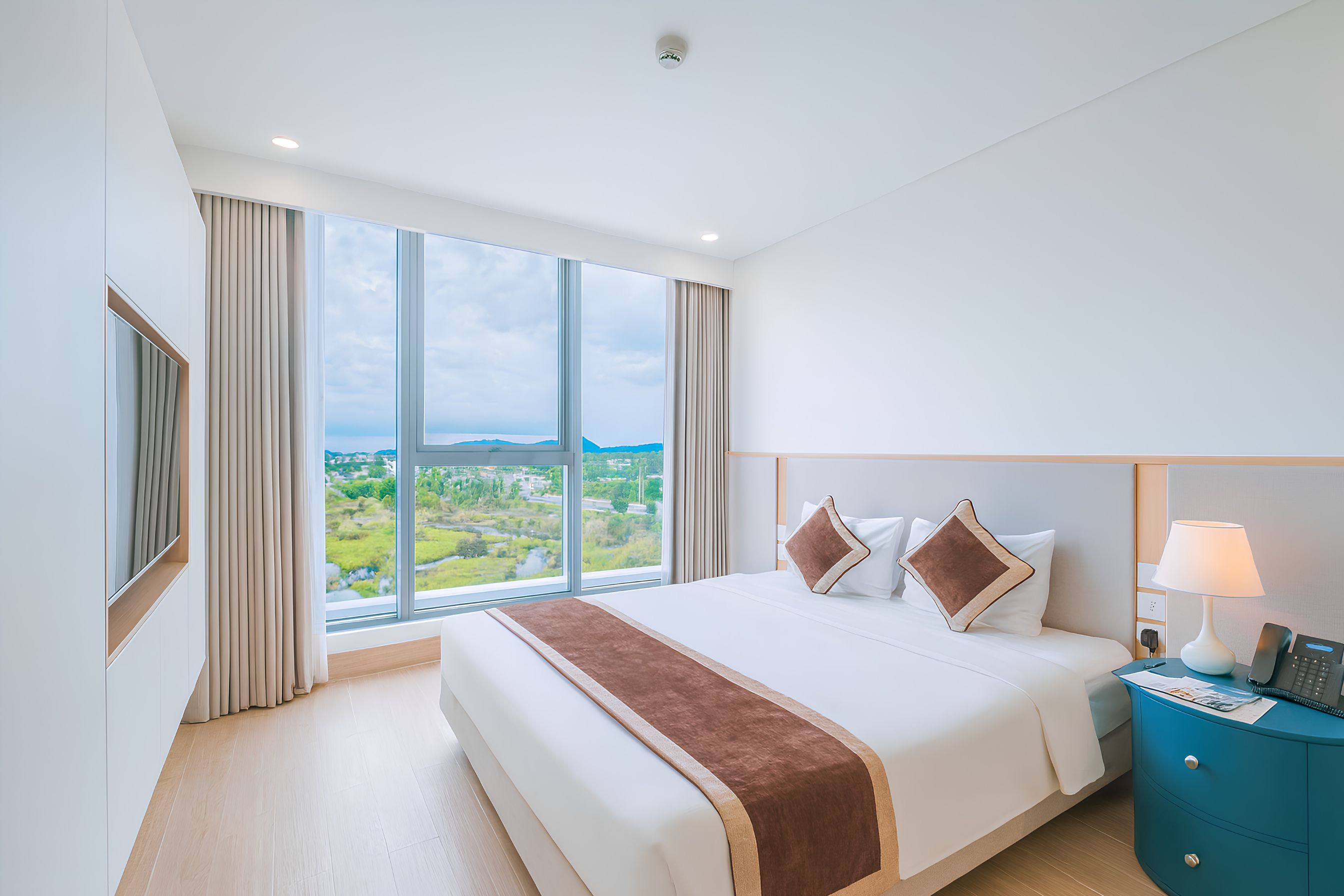 Habitación de hotel con una cama grande, una mesita de noche, una lámpara y vistas al paisaje a través de la ventana.