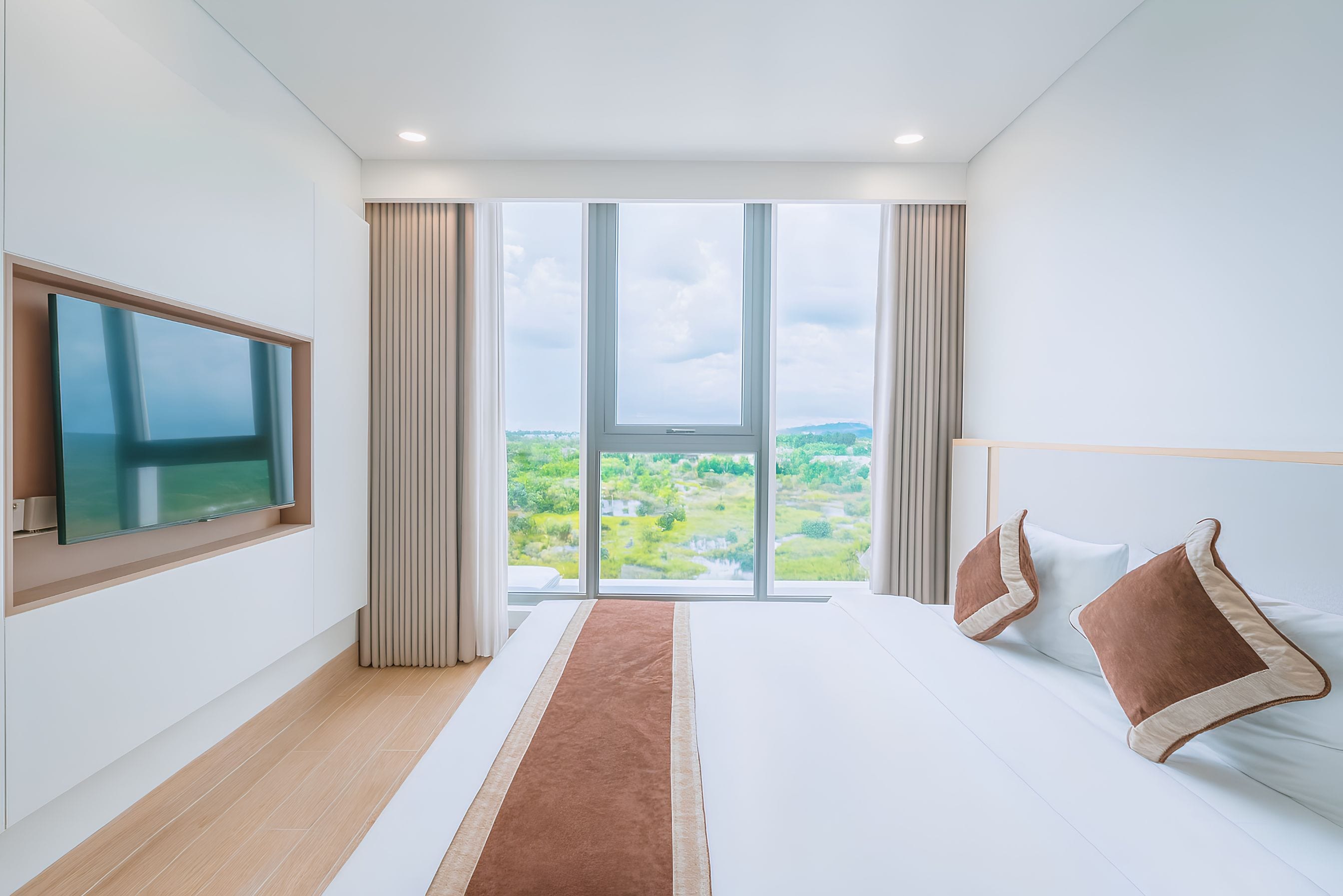 Un dormitorio moderno con un ventanal grande, un televisor de pantalla plana y una cama con almohadas marrones.