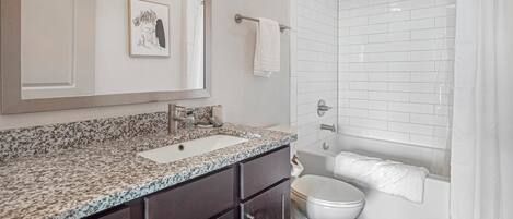 Un baño con encimera de granito, un lavabo blanco, inodoro y ducha con puerta de vidrio.