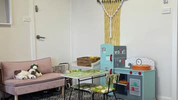 Une pièce avec un canapé, une petite table, des chaises, une cuisine miniature pour enfants et un rideau.