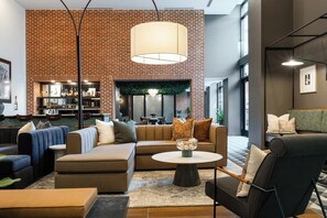 A modern lounge area with sofas, a coffee table, and a brick wall. - Landing | Beautiful 1BD, Rooftop Lounge (Richmond)