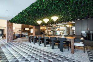 A modern kitchen with a green leafy wall, a dining area with a geometric patterned floor, and a bar area with a brick column. - Landing | Chic 1BD, Rooftop Lounge (Richmond)