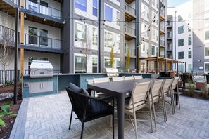 En moderne udendørs terrasse med grill, spisebord og stole.